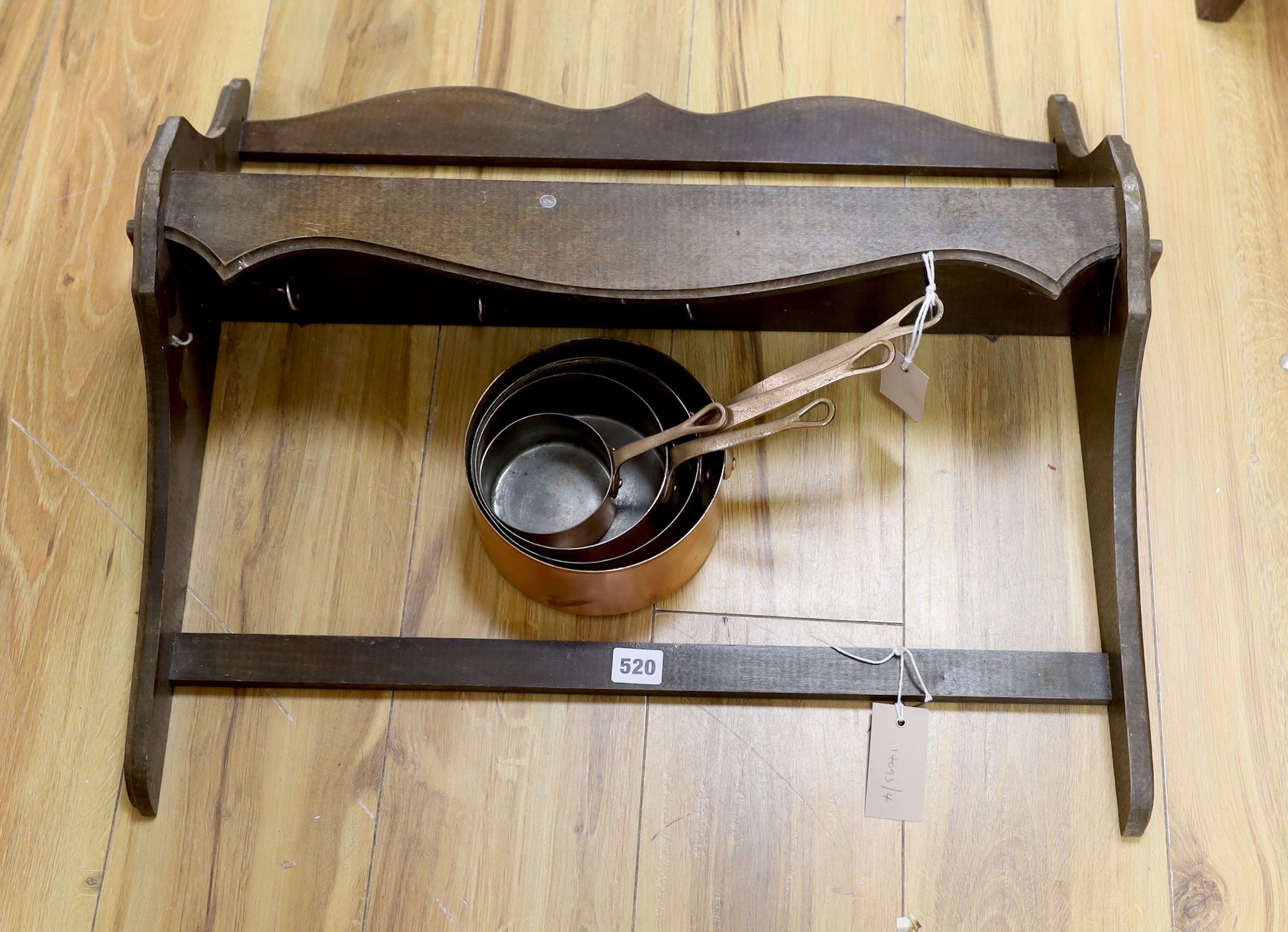A graduated set of four copper and brass handled saucepans with a beech hanging wall rack, rack approximately 64cm wide